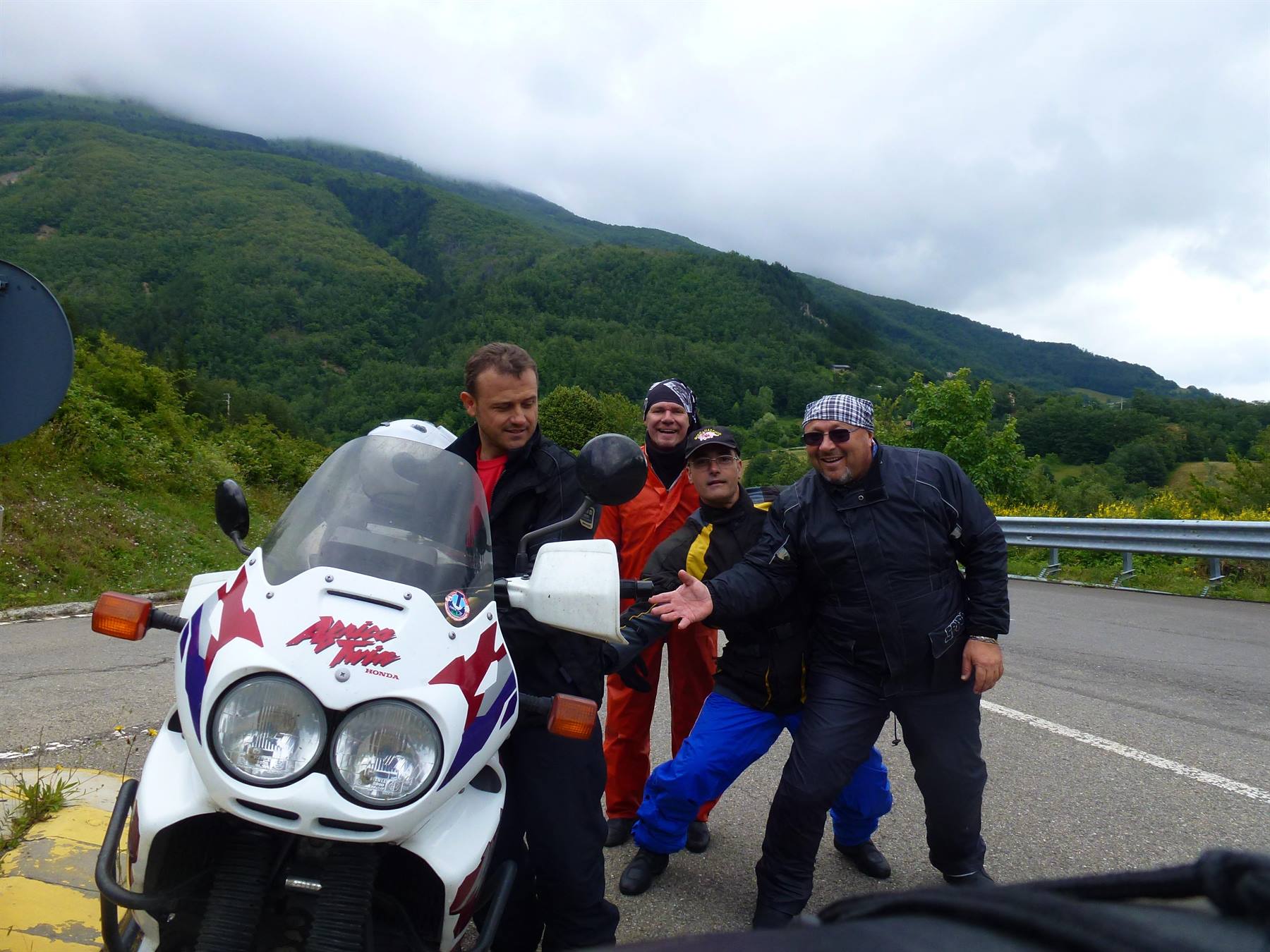 Quattro motociclisti accanto a una BMW bianca su strada di montagna