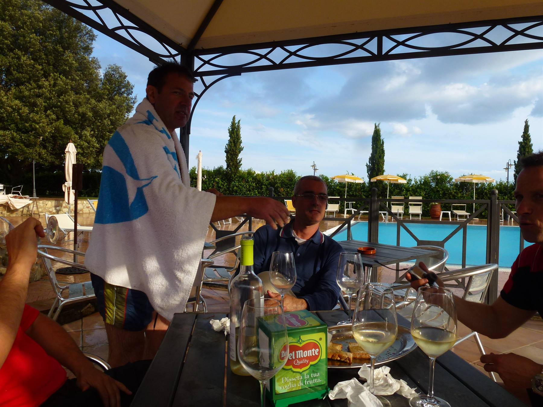 Uomini brindano con vino bianco al tavolo accanto alla piscina, uno con l'asciugamano