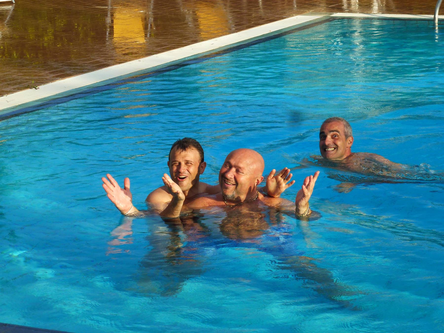 Tre uomini sorridenti giocano nell'acqua blu di una piscina