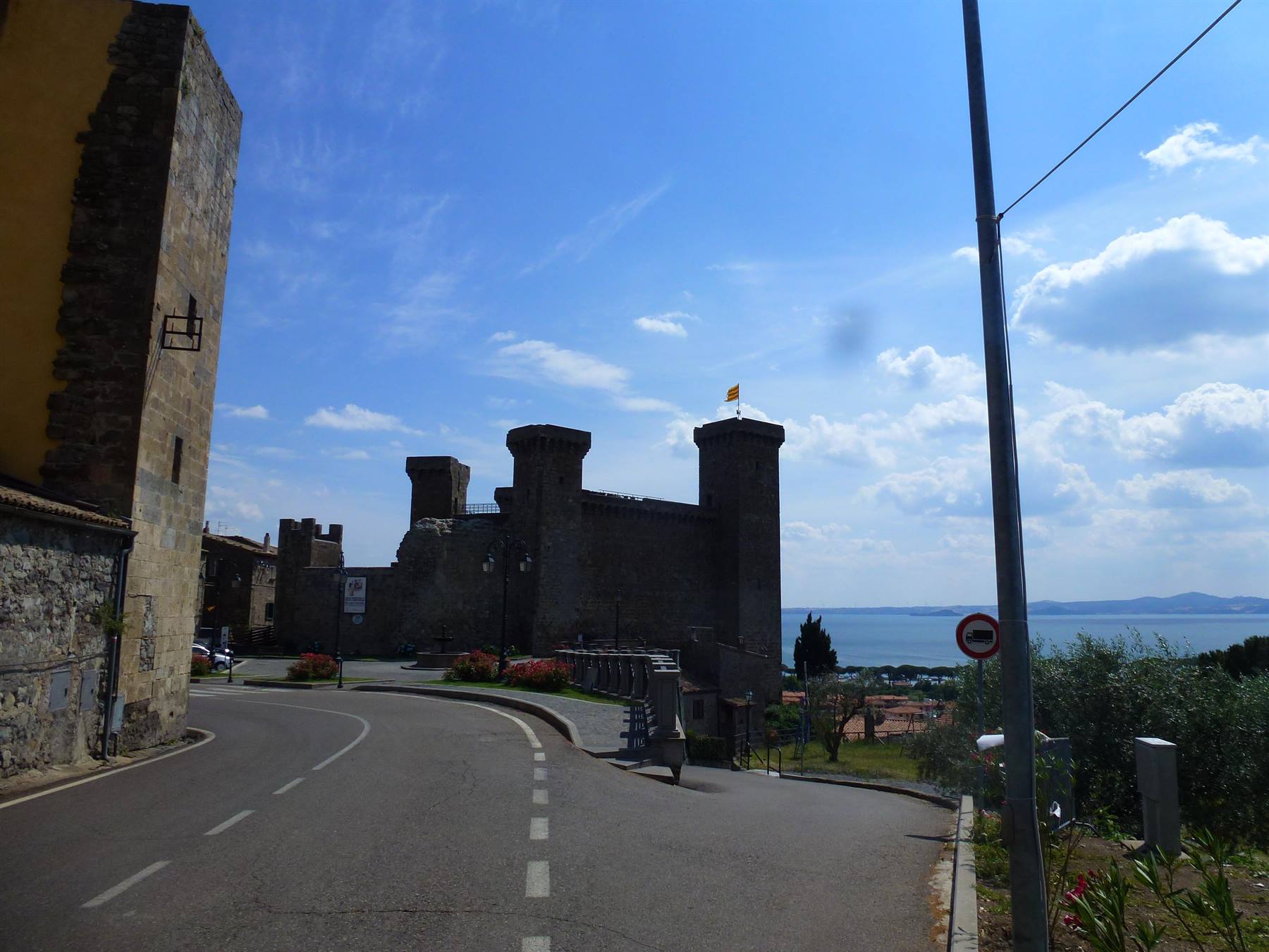 Rocca medievale in pietra sopra il lago, strada che sale, cielo azzurro