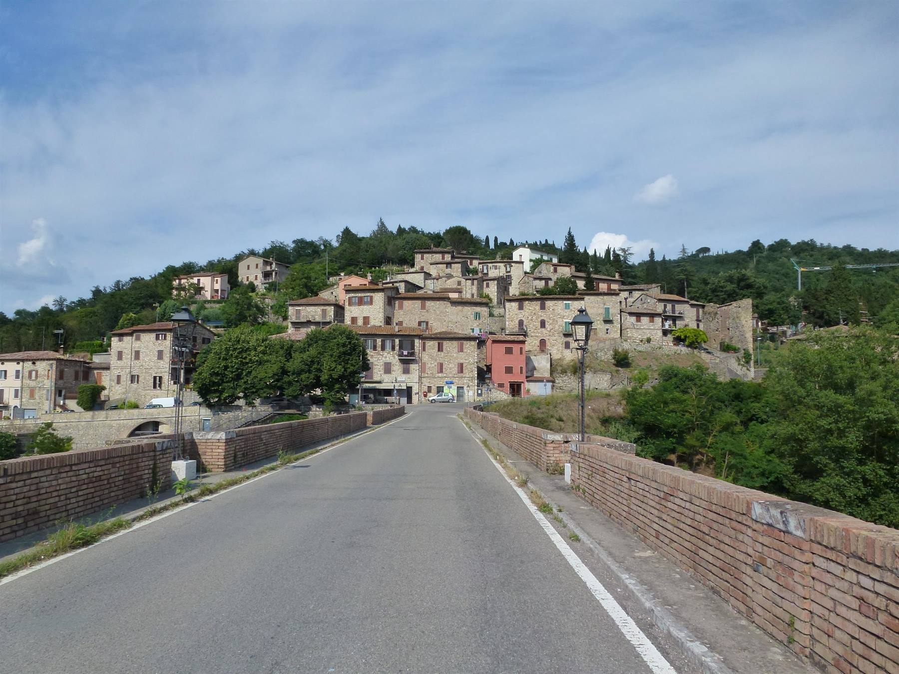 Strada su ponte in mattoni verso borgo medievale di case in pietra sulla collina