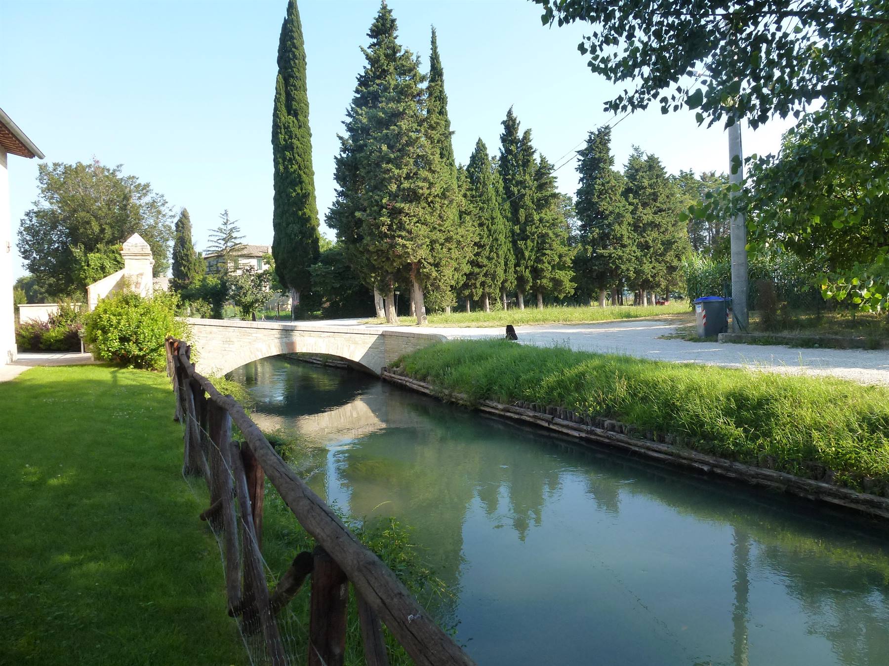 Ponte in pietra su canale verde circondato da cipressi e prato