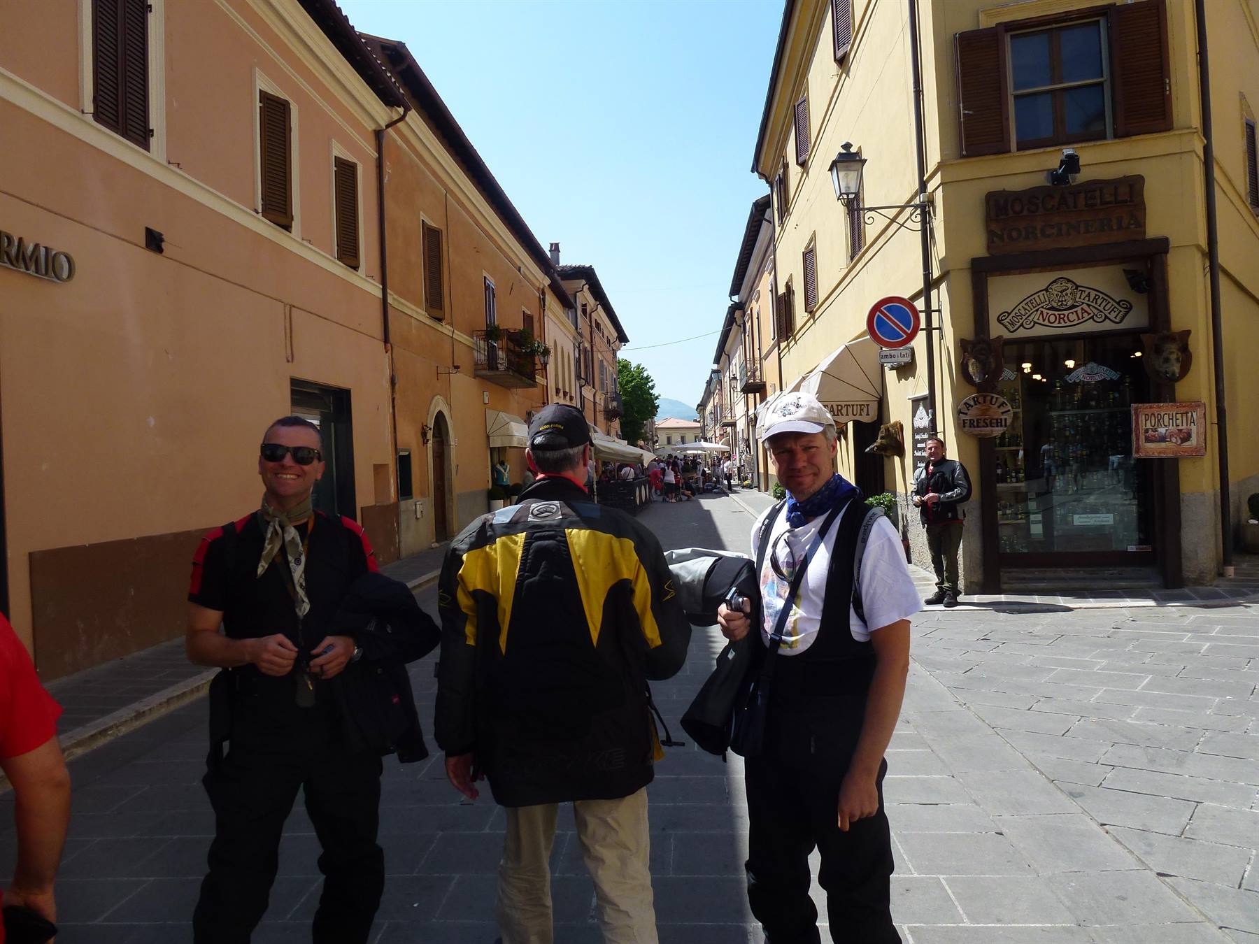 Tre motociclisti in tuta siedono in una strada lastricata con case colorate