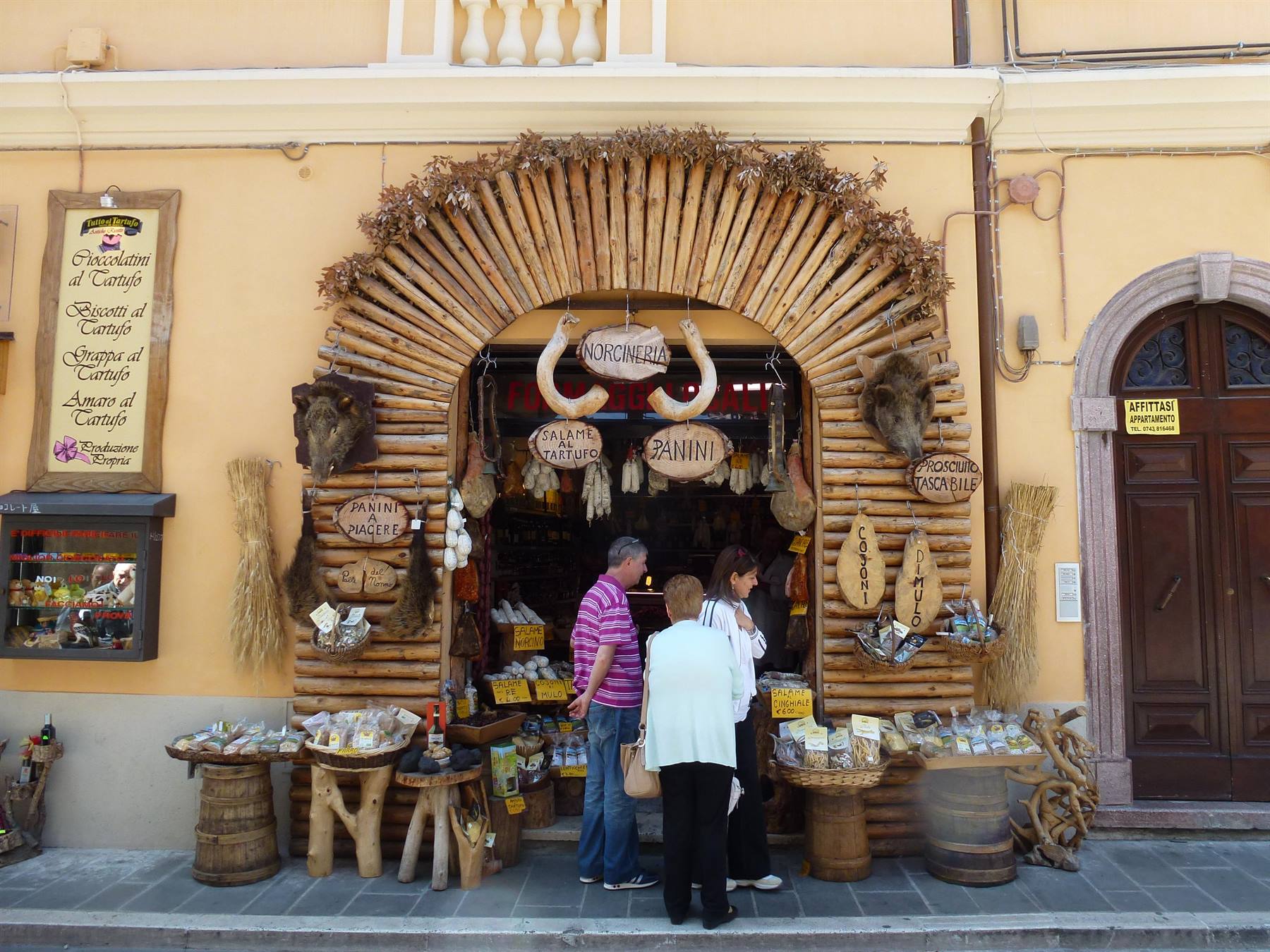 Turisti davanti a un negozio di alimentari con facciata di legno e salumi appesi