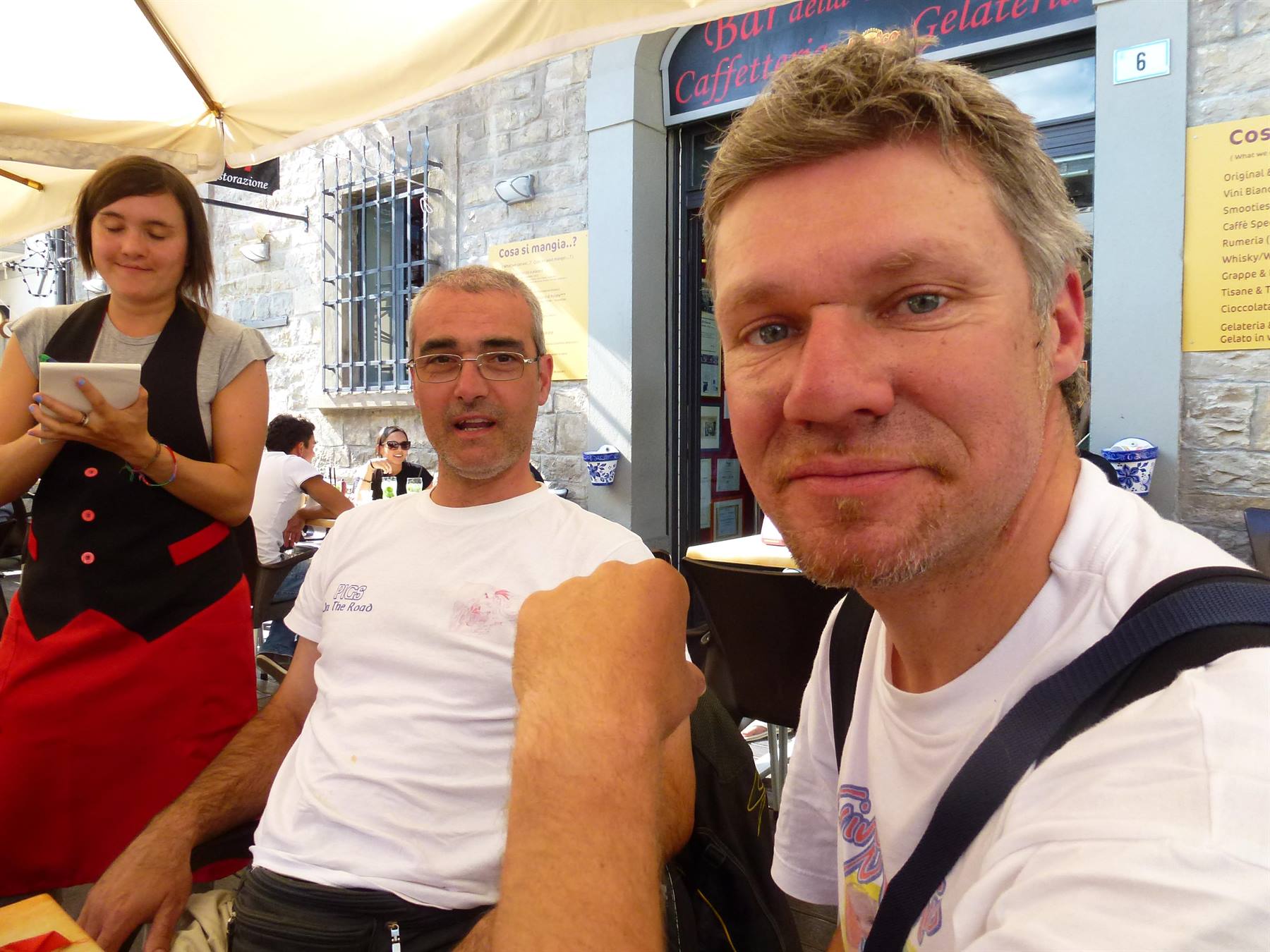 Selfie di due uomini in t-shirt bianche al bar Gelateria, ombreggiati dal tendone