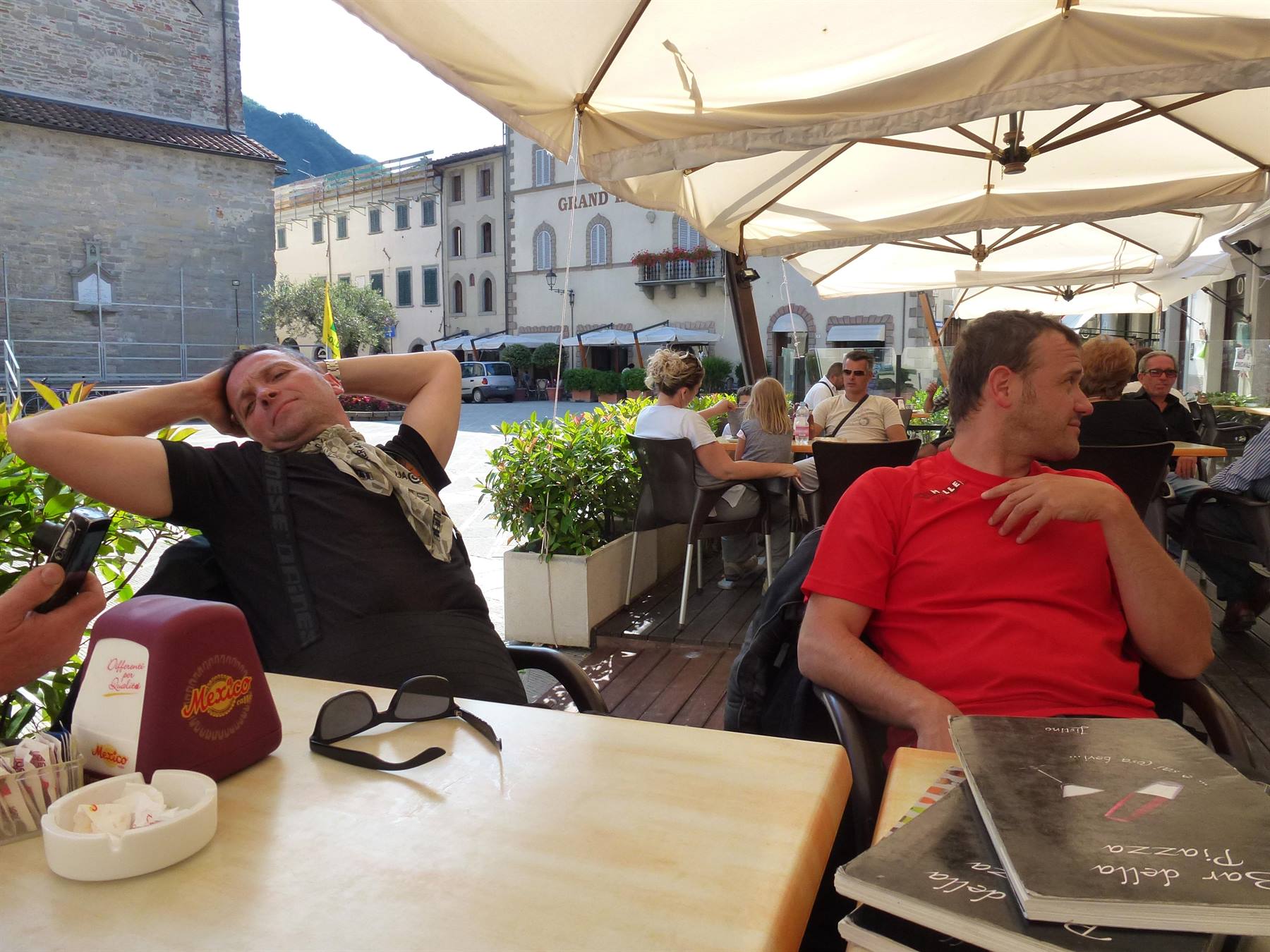 Turisti rilassati ai tavolini del Bar della Piazza sotto ombrelloni, piazza con palazzi antichi
