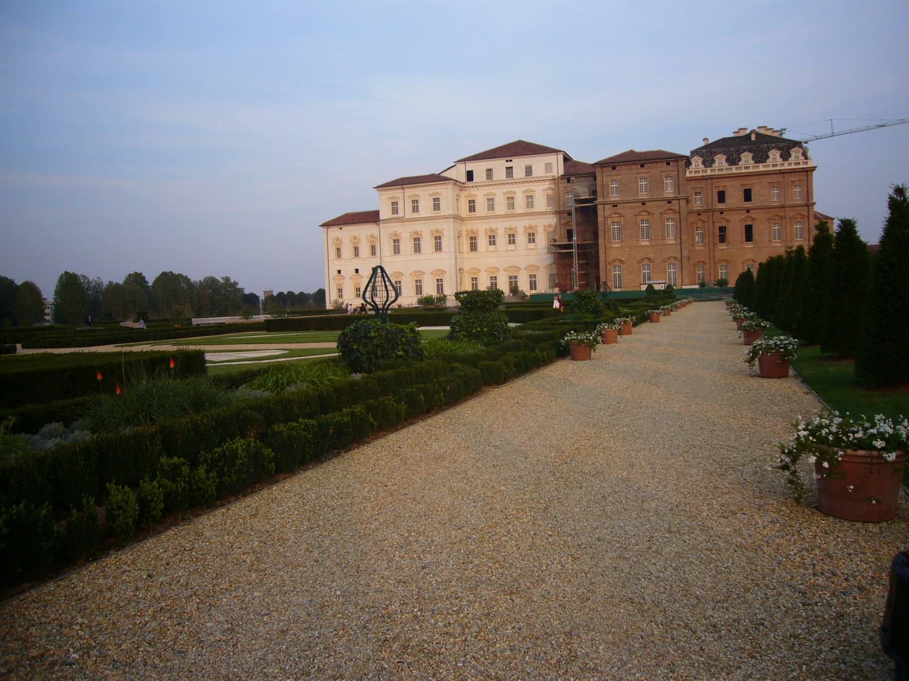 Viale ghiaiato nei giardini della Reggia di Venaria, vasi di fiori e palazzo illuminato