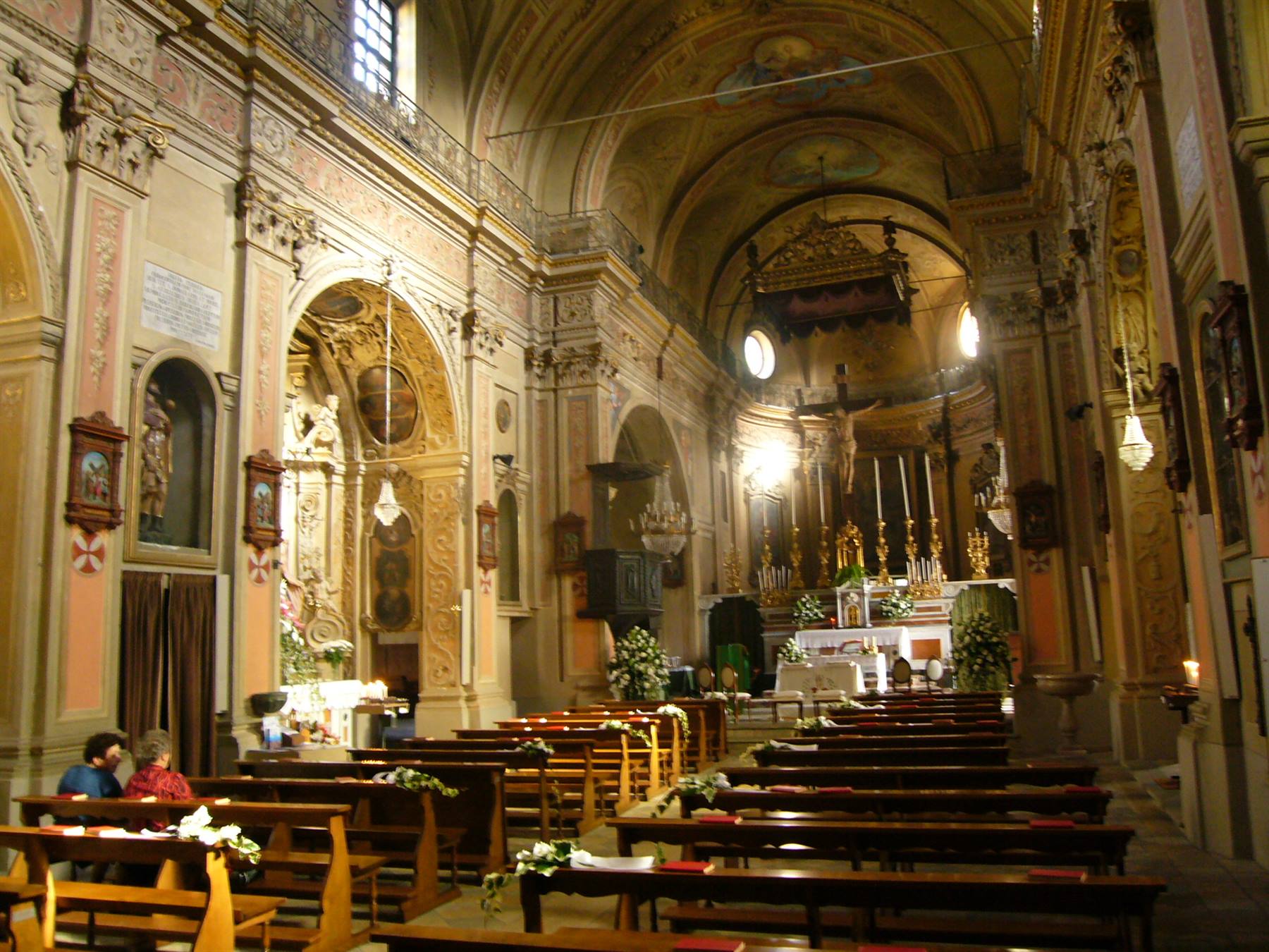 Navata di chiesa barocca con altare decorato per un matrimonio, panche in legno e luce naturale