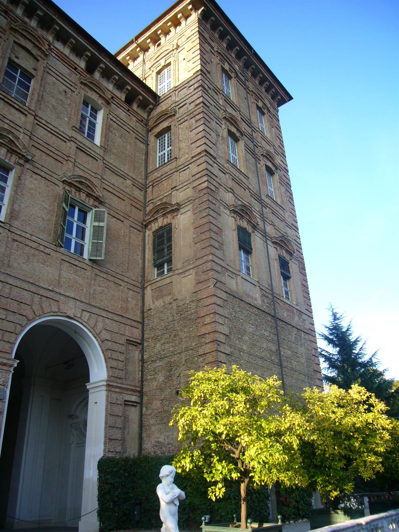 Torre in mattoni del Palazzo Ducale di Modena, sole del mattino, statua e agrumi in giardino