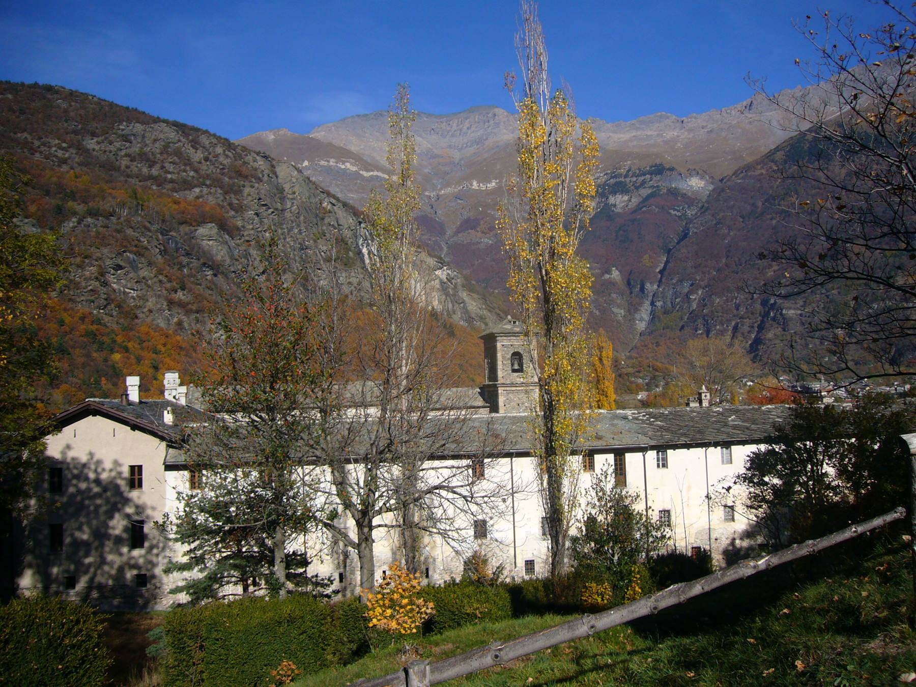 Monastero con campanile tra alberi autunnali e montagne, Aosta