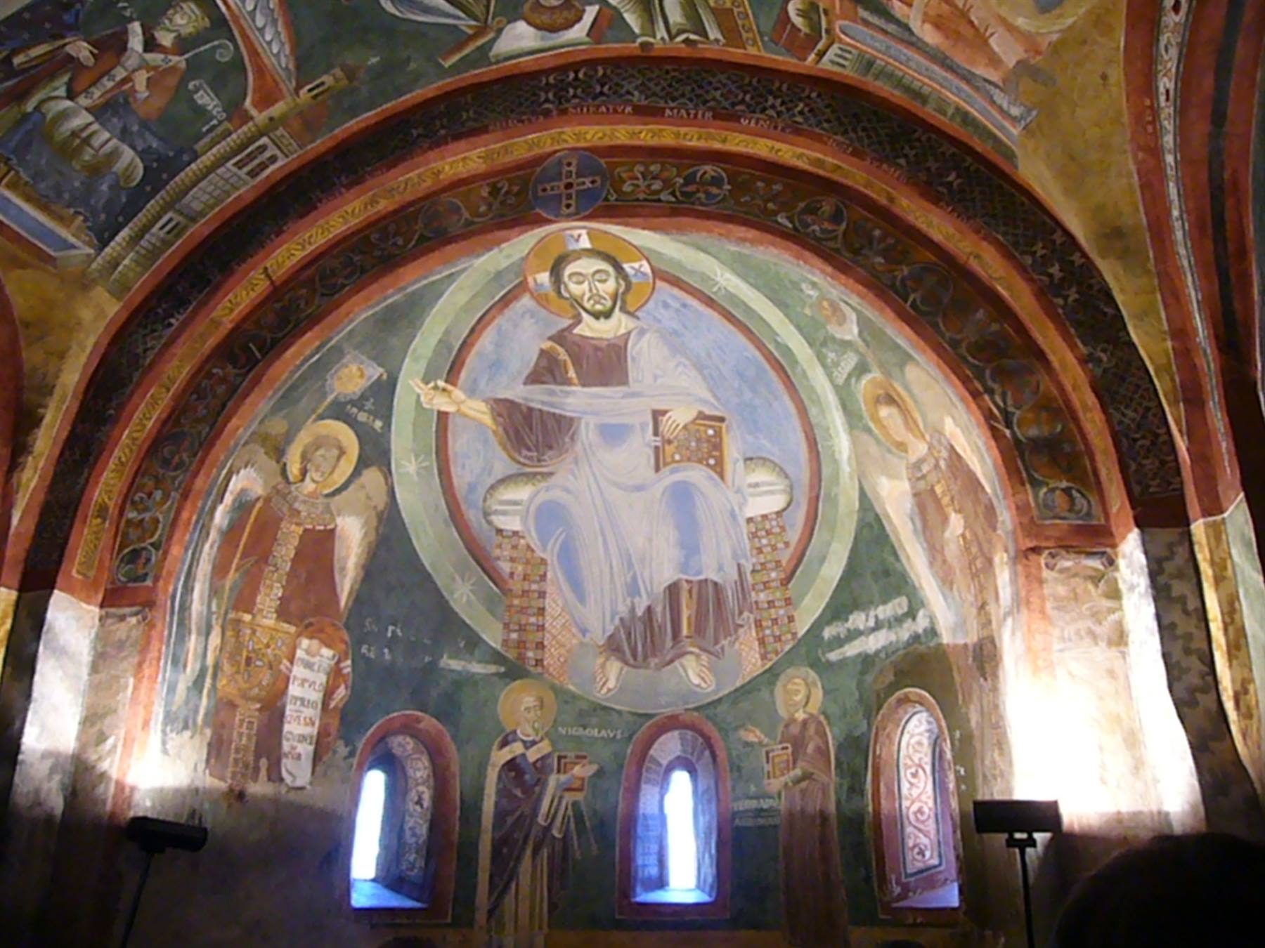 Affresco di Cristo in trono dentro una chiesa medievale illuminata da lampade