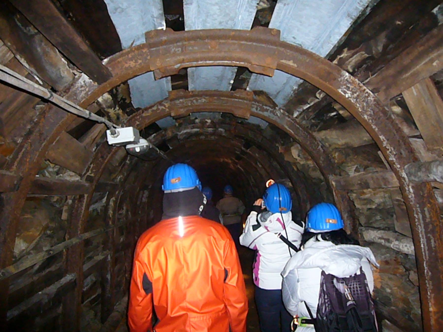Visitatori con caschi blu attraversano una galleria mineraria con archi in acciaio arrugginito