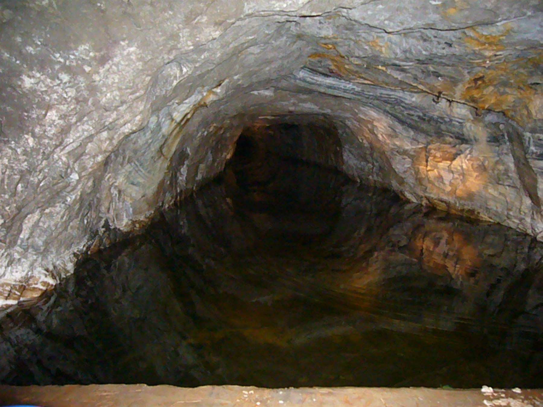 Galleria scavata nella roccia con acqua scura, illuminata artificiale sui moli