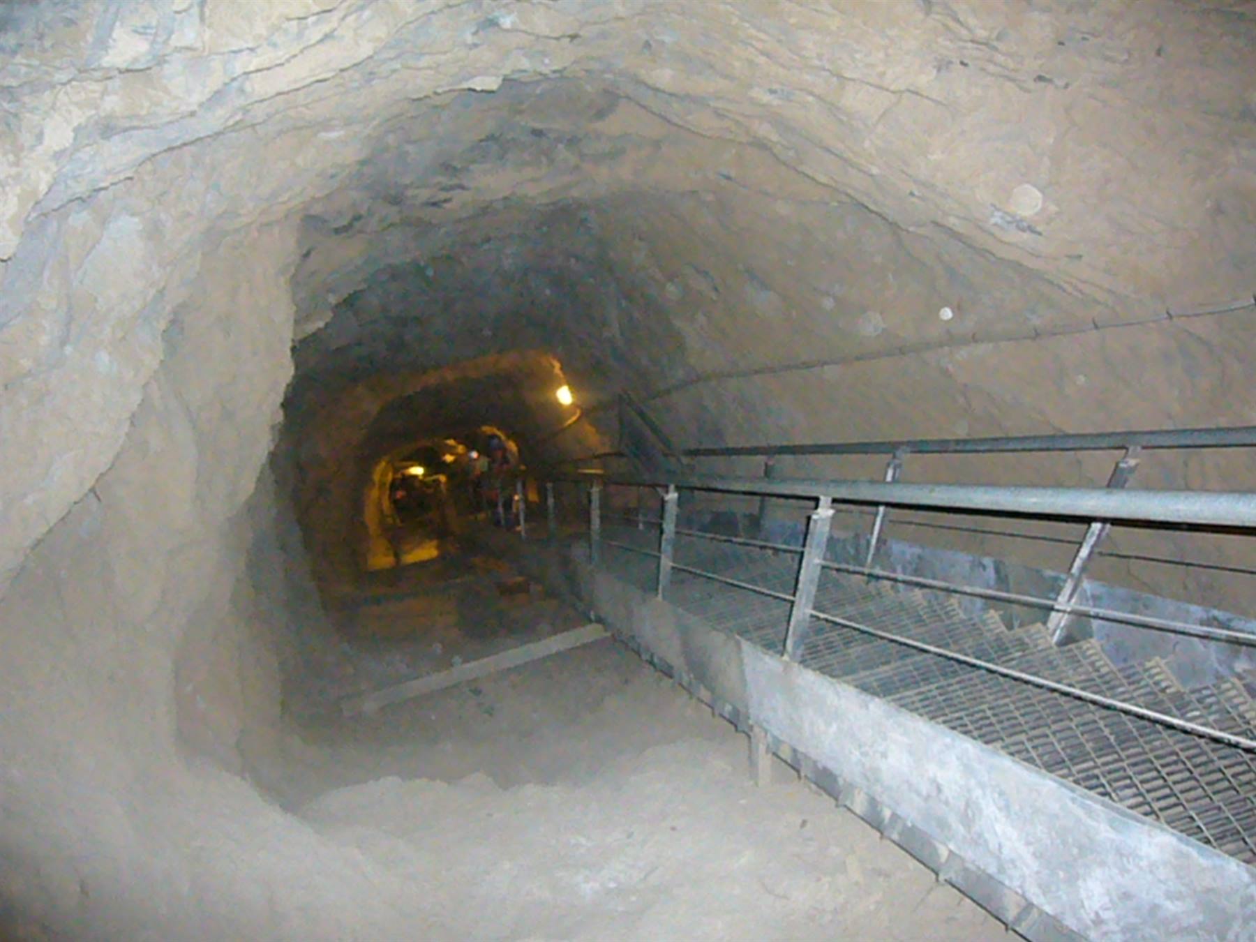 Galleria scavata nella roccia con passerella in metallo e luci sparse