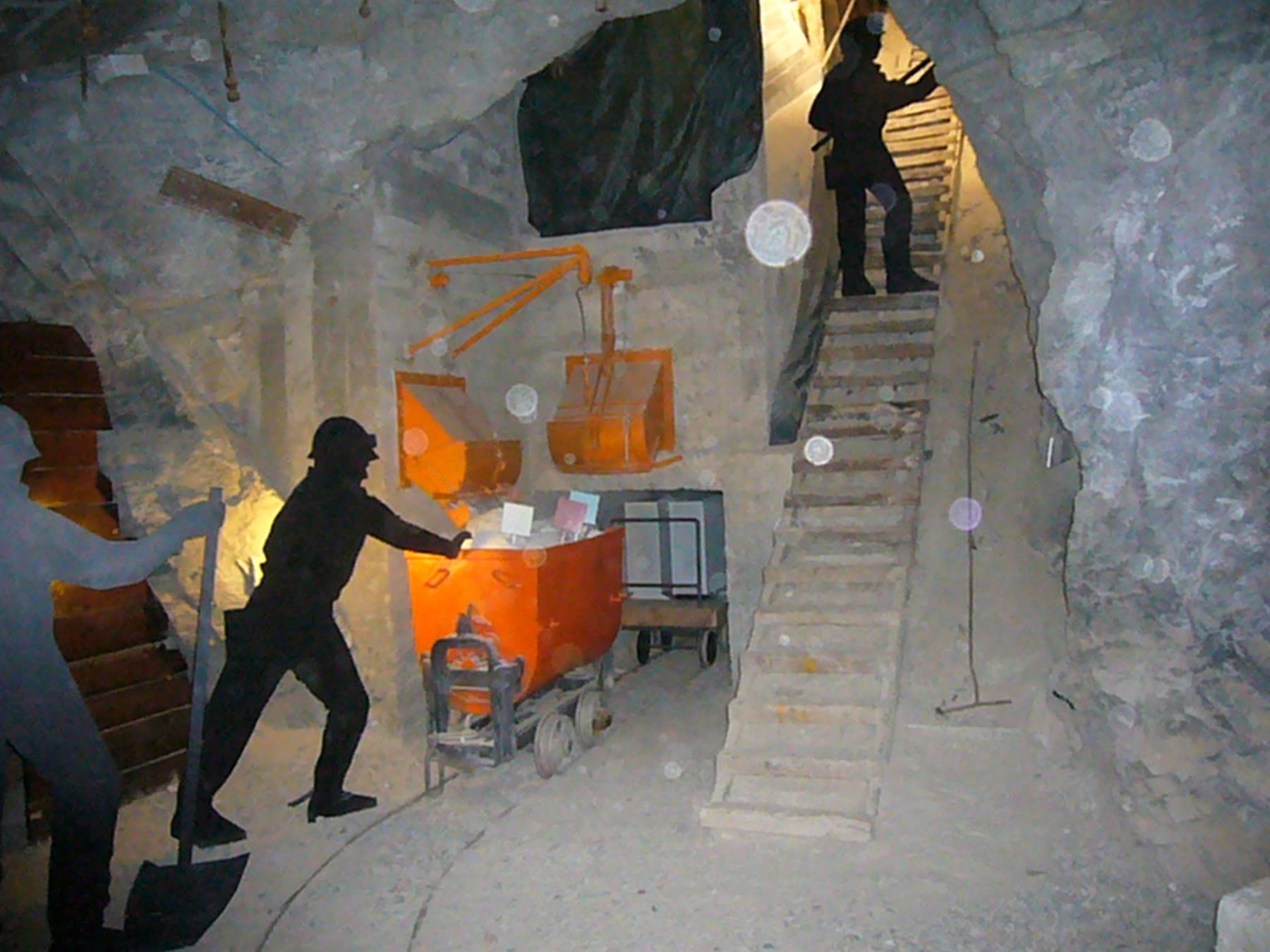 Minatori manichino con carrello arancione in galleria mineraria con scale