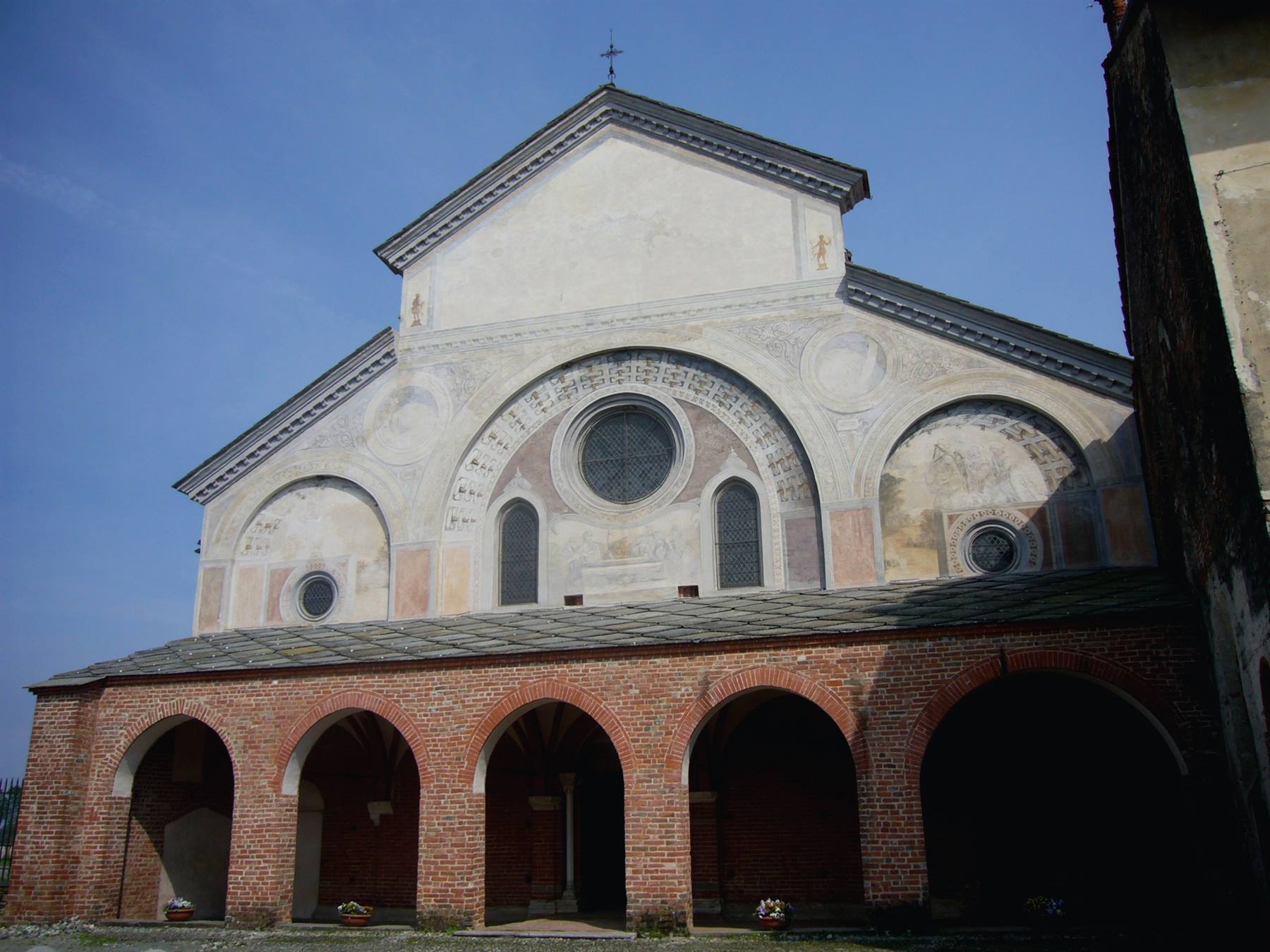 Facciata romanica con rosone e archi, portico in mattoni sotto cielo azzurro