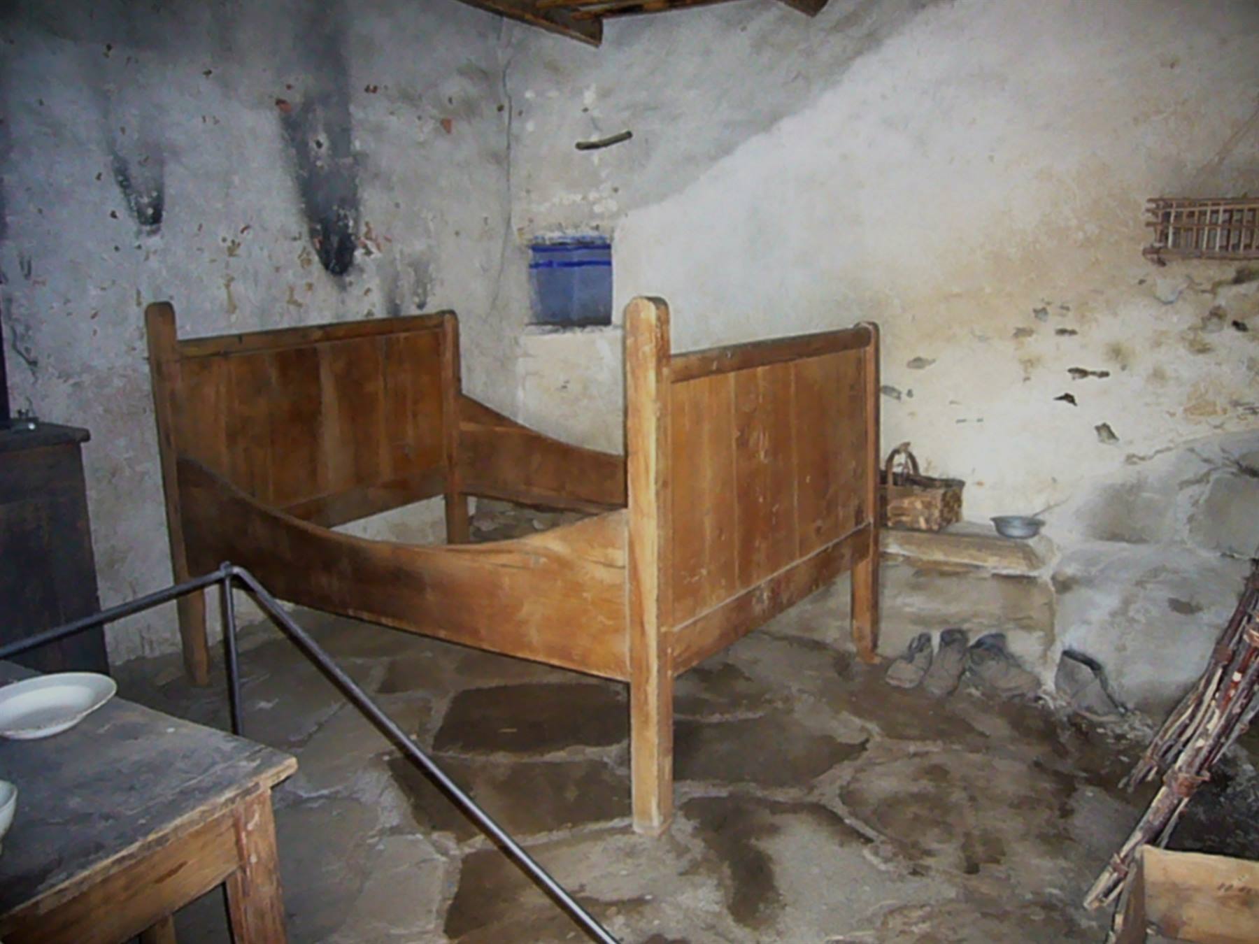 Letto in legno antico in una stanza rurale con muri intonacati e pavimento in pietra
