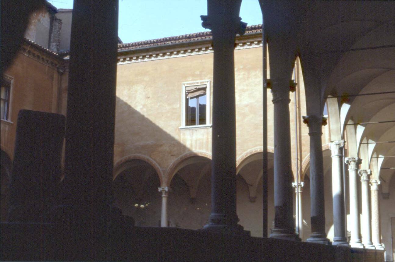 Chiostro con colonne in pietra e archi, luce solare sulla facciata ocra