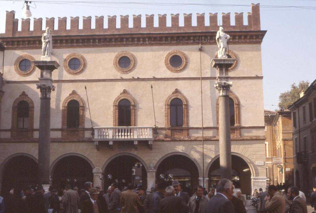 Palazzo comunale con merlature e statue su colonne, folla in piazza a Ravenna
