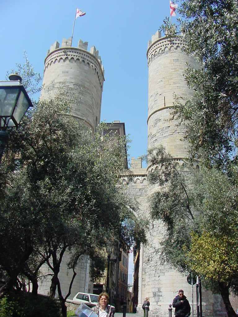 Turiste camminano sotto le due torri medievali di pietra di Porta Soprana a Genova