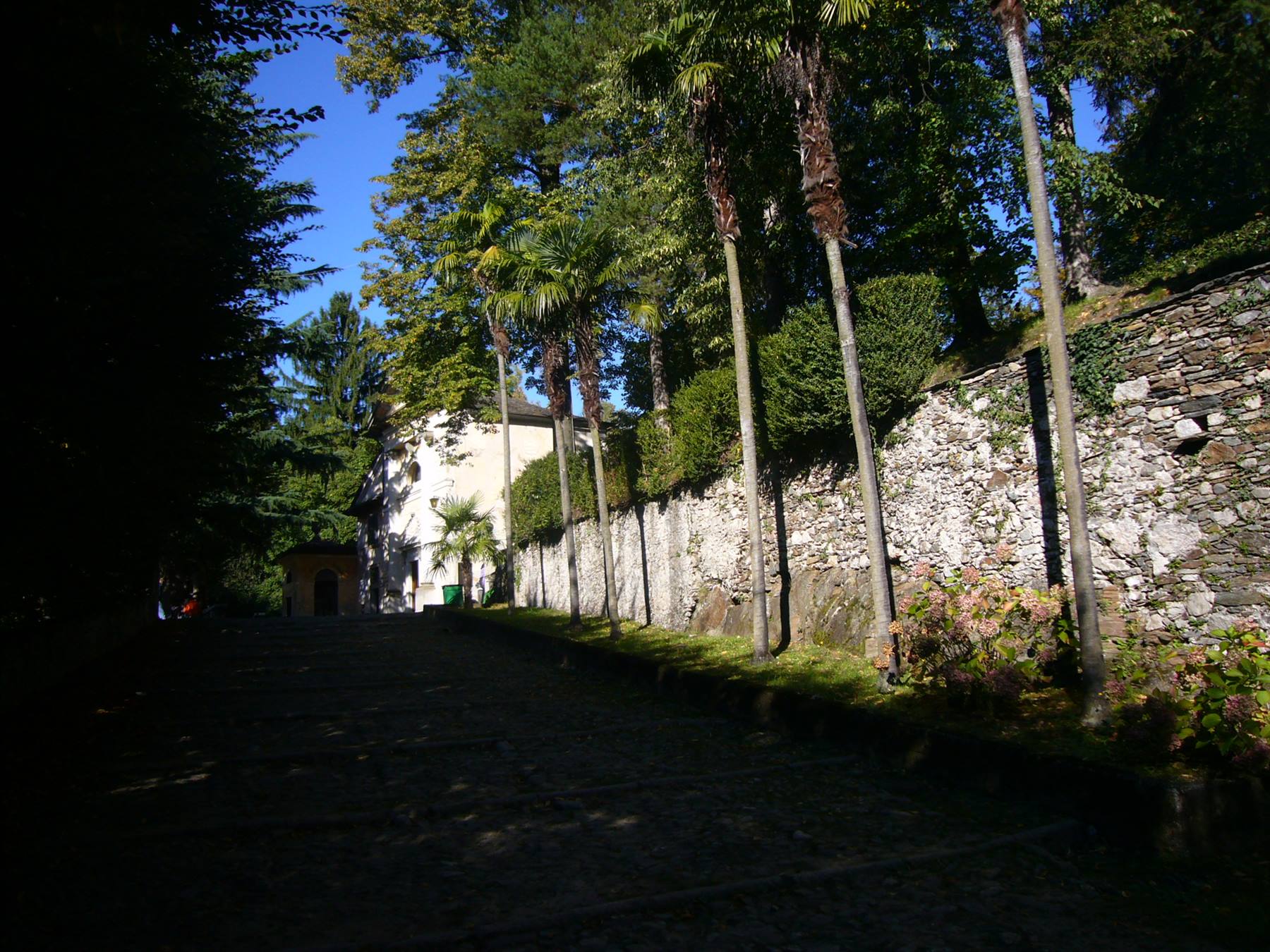 Viale alberato in pietra accanto a muro antico e cappella bianca, luce solare