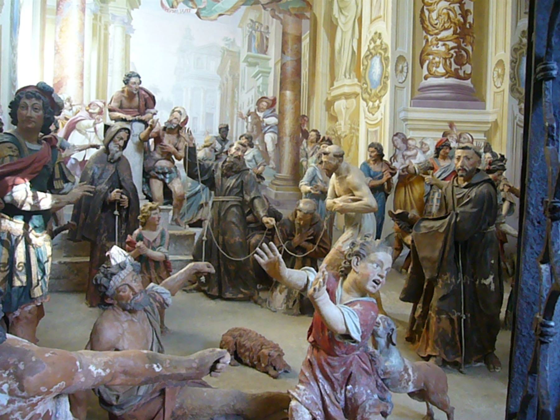 Cappella con statue dipinte a grandezza naturale, monaci in abiti scuri fra figure agitate