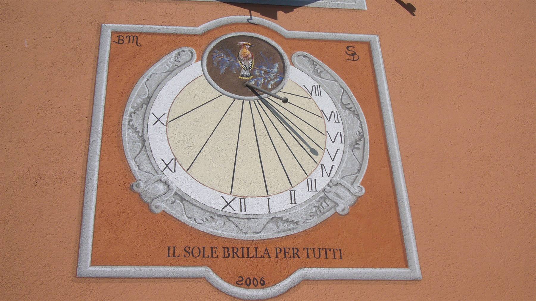 Meridiana dipinta su muro ocra, numeri romani, motto 'Il sole brilla per tutti'
