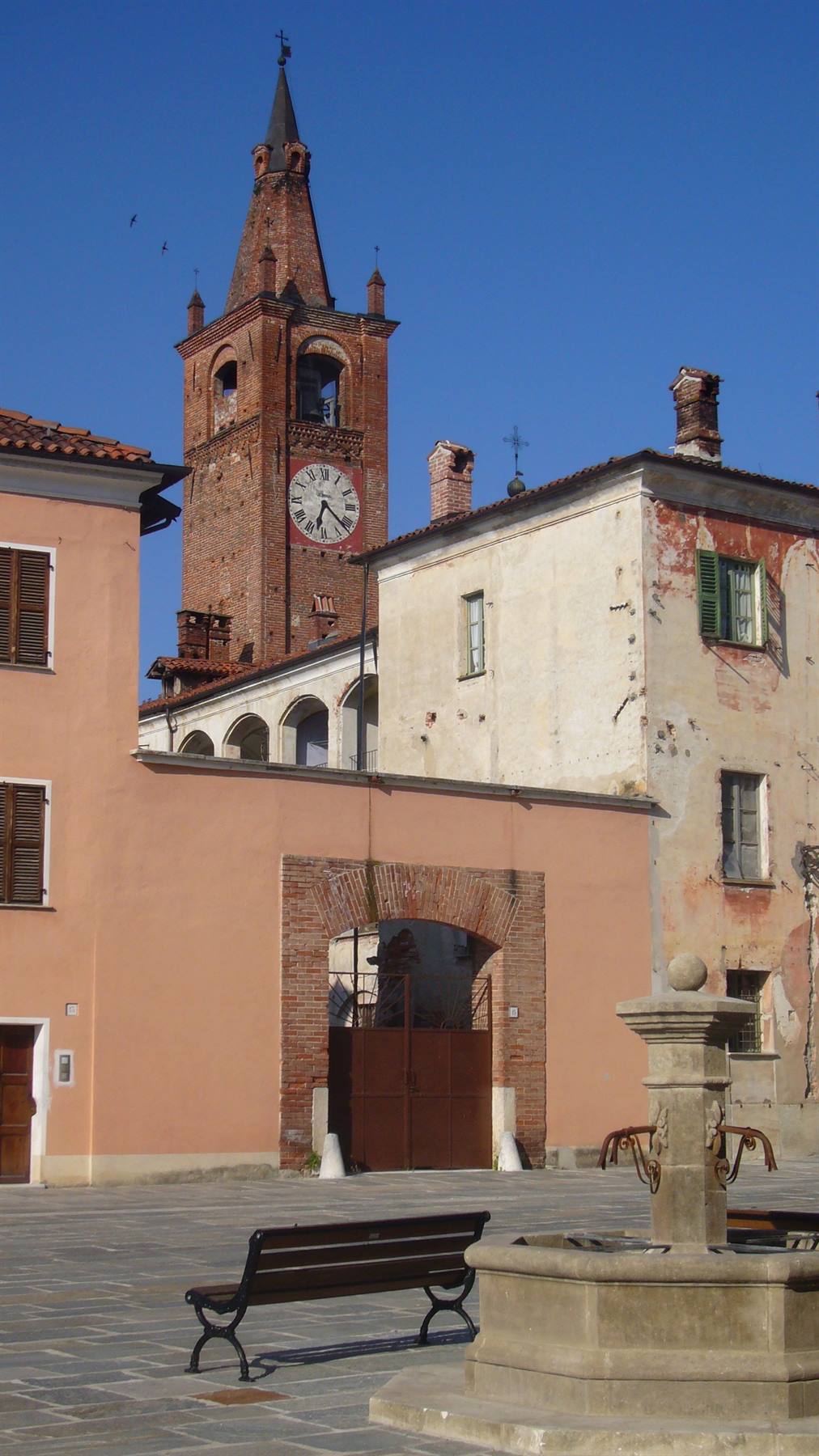 Campanile in mattoni con orologio su piazza, panchina e fontana di pietra