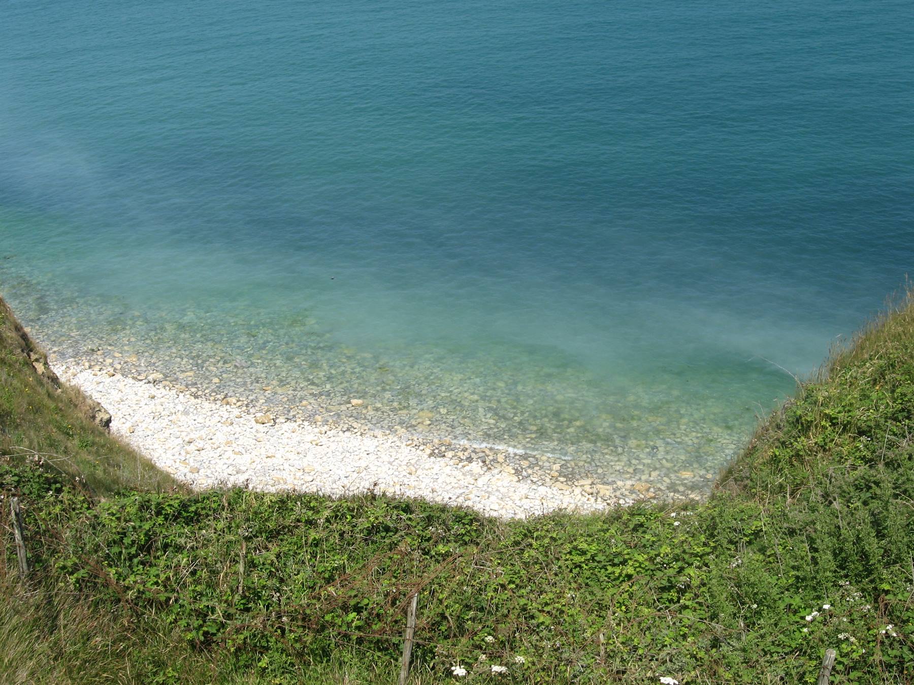 Piccola caletta con ciottoli bianchi, mare verde acqua e pendii erbosi