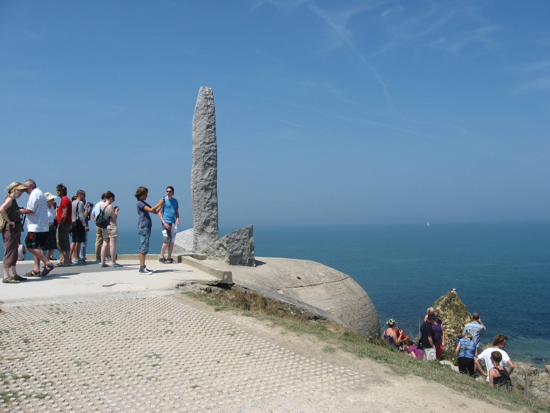 Turisti accanto a un monolite di pietra sul promontorio di Pointe du Hoc