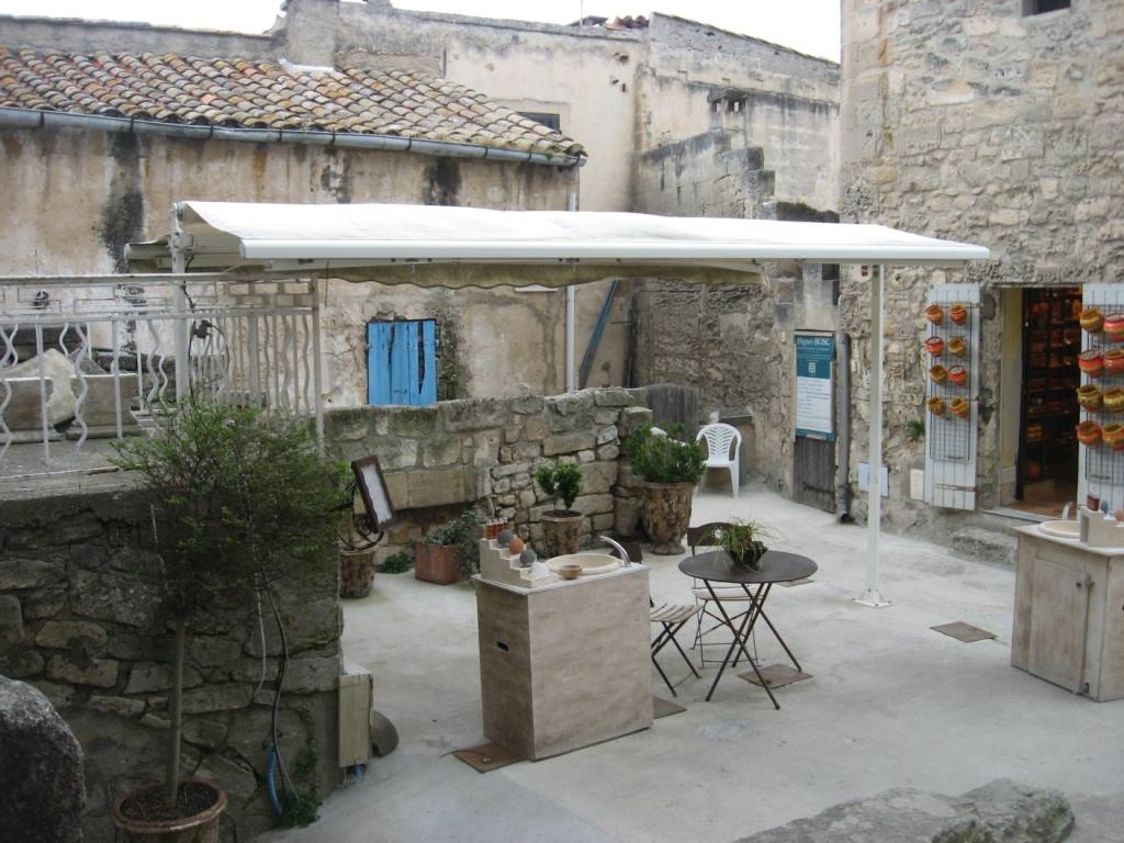 Cortile in pietra con tettoia bianca, tavolino e vasi tra case rustiche, Les Baux