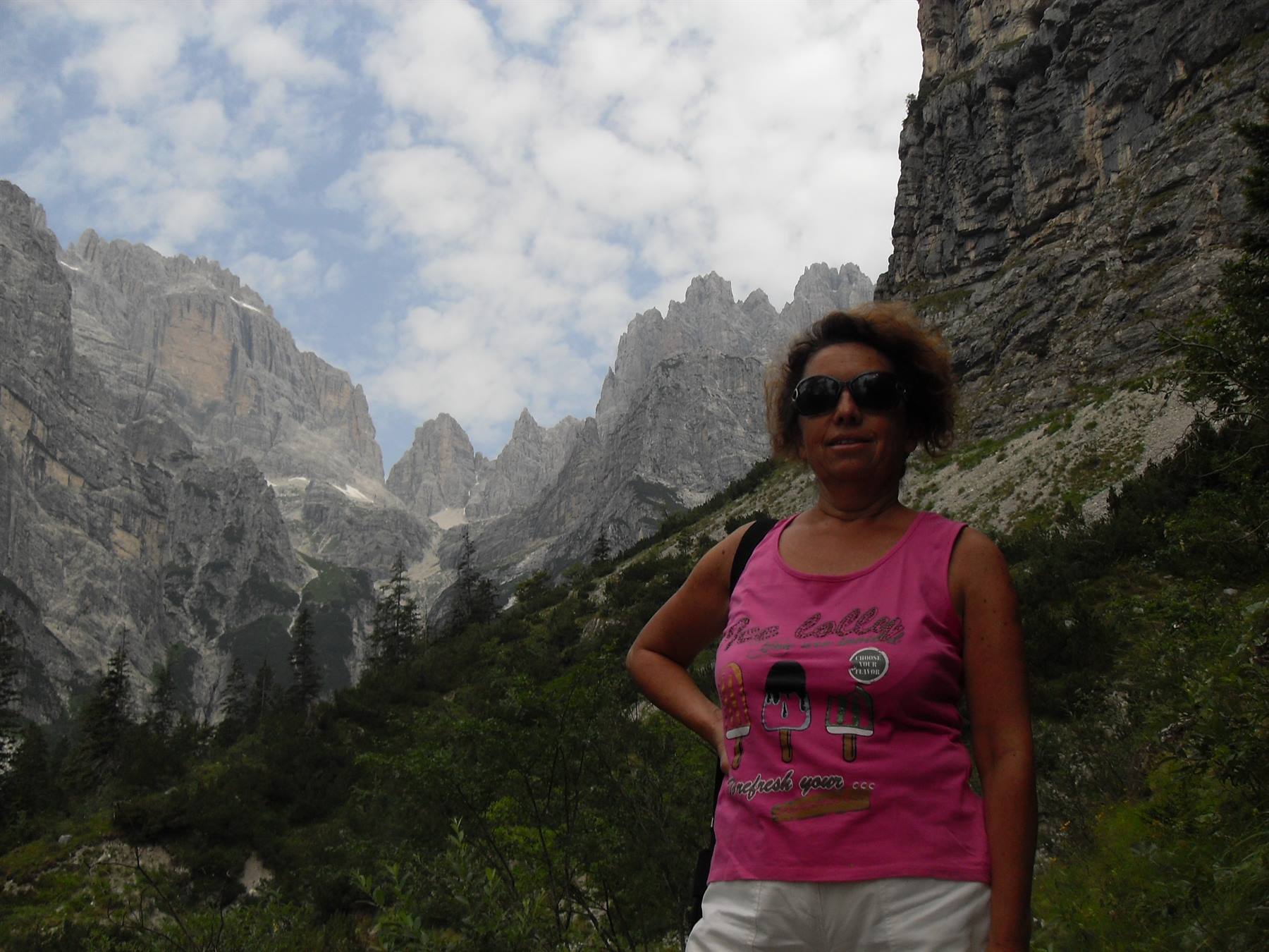 Donna in canotta rosa con occhiali davanti alle pareti rocciose dolomitiche