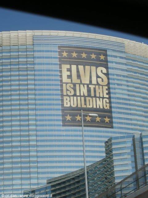 Grattacielo di vetro con enorme banner blu e oro che dice "Elvis is in the building"