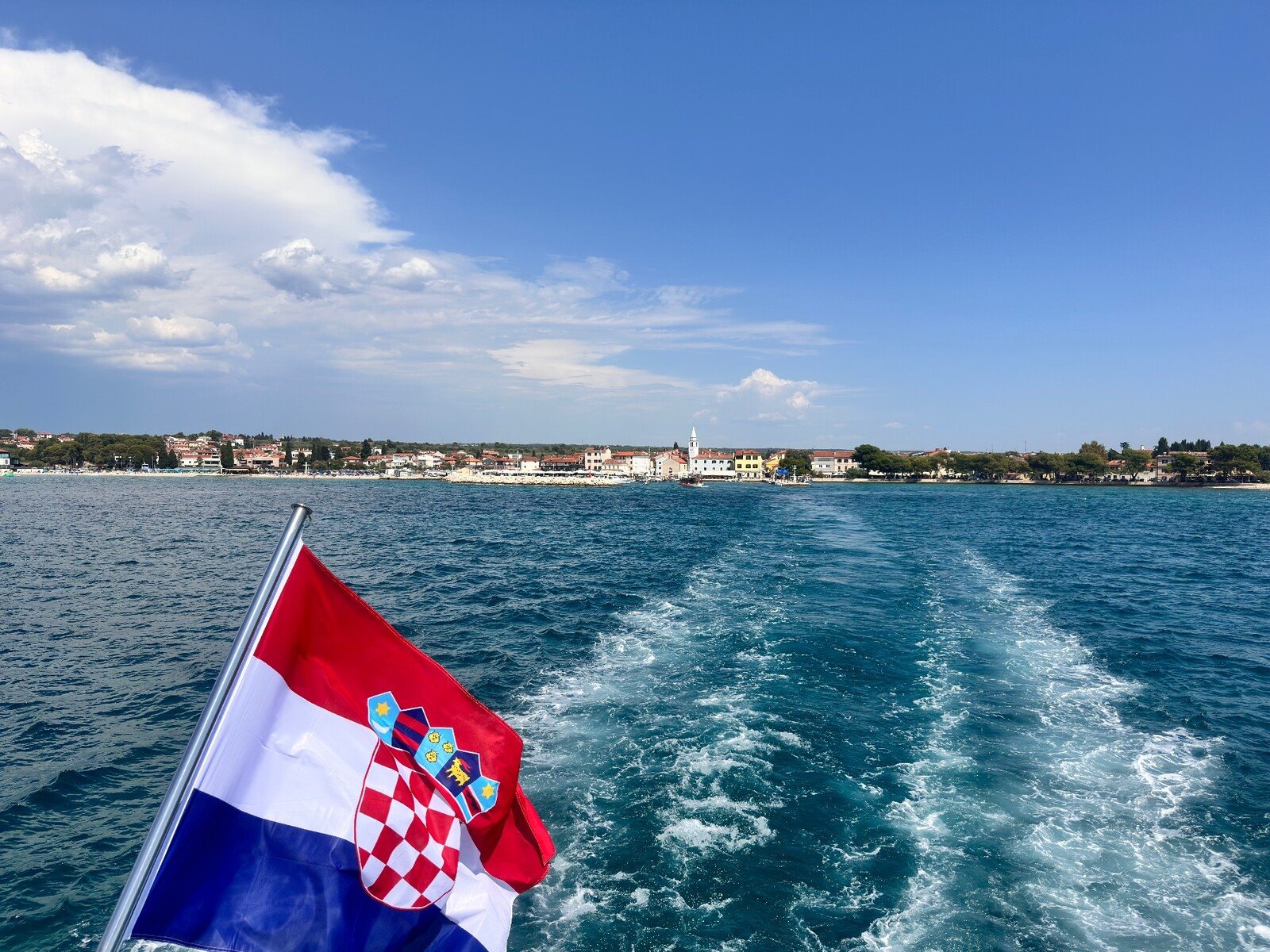 Addio alla costa istriana: la scia del traghetto e la bandiera croata al vento.