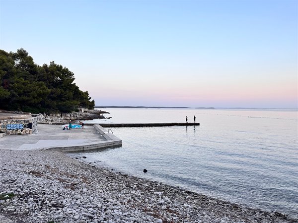 Tramonto rosa sul mare, cieli tenui dal pontile di Zadar.