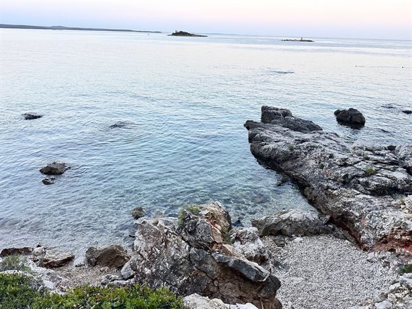 Tramonto quieto sul mare cristallino tra gli scogli, un momento sospeso.