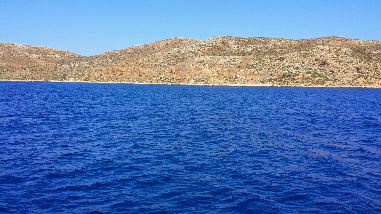 Navigando verso coasta selvaggia, mare blu infinito e sole caldo.