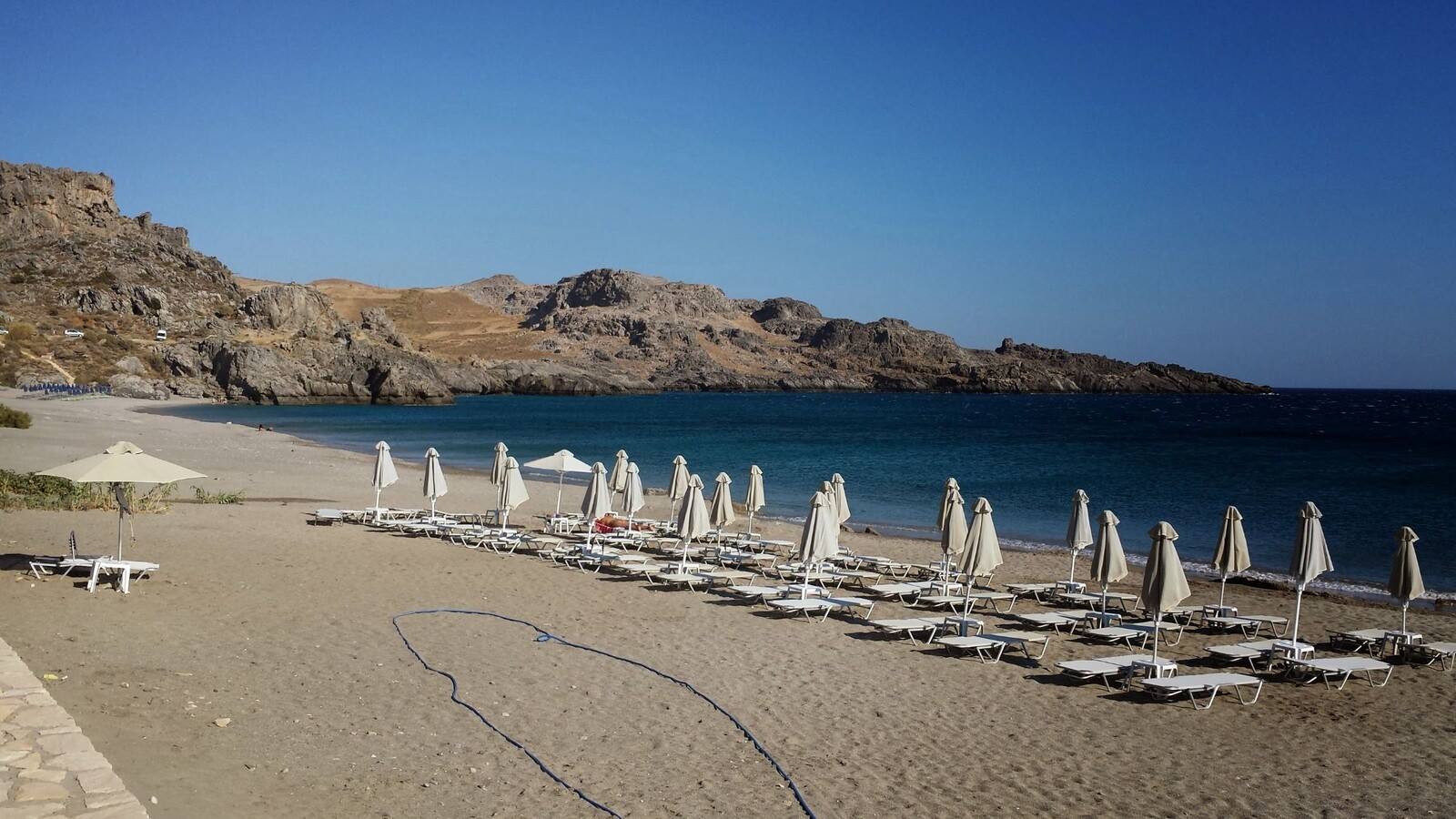 La baia di Lindos al mattino, ombrelloni chiusi in attesa di mattinate pigre.