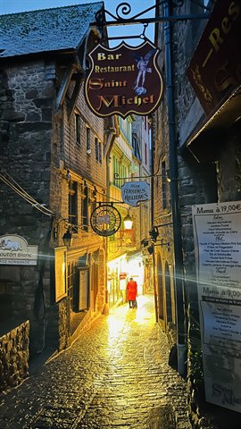Vicolo bagnato di pioggia e luce dorata: sera magica al Mont Saint-Michel.