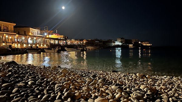 Una sera di luna piena, la spiaggia di sassi brilla sotto le luci del borgo.