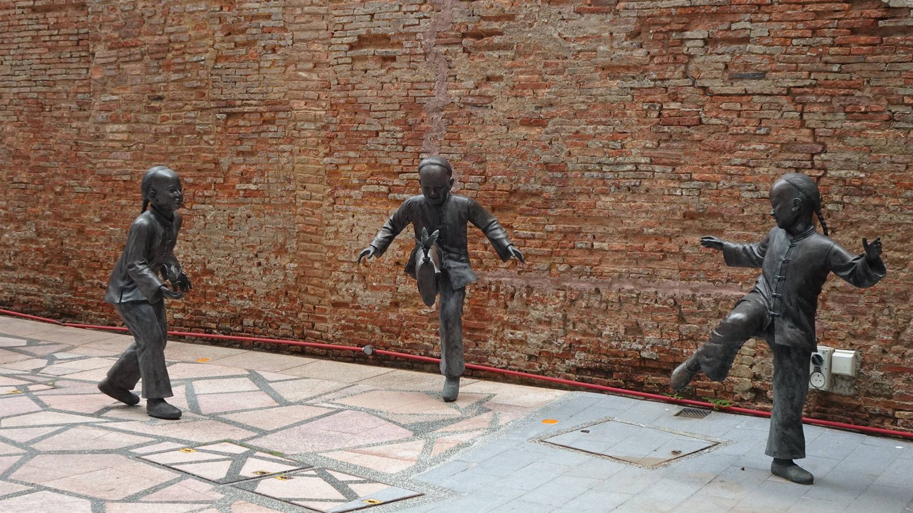 Bambini di bronzo giocano per sempre contro il muro antico.