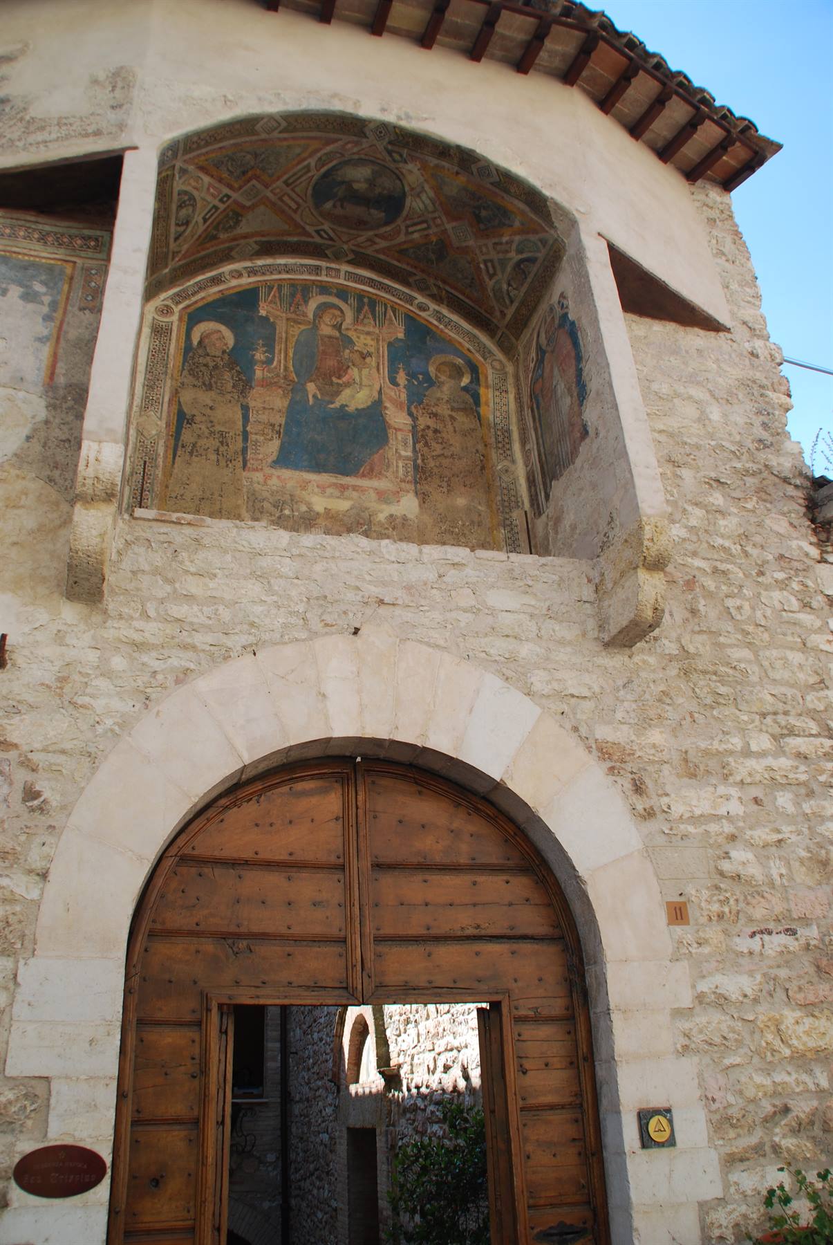 Affresco medievale sopra portale in legno di pietra chiara, luce solare