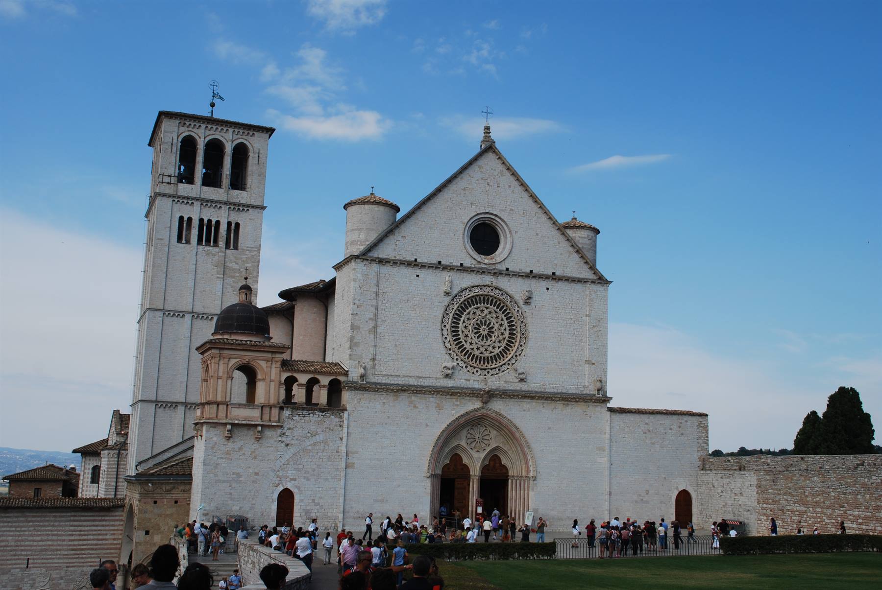 Facciata bianca della Basilica di San Francesco ad Assisi con rosone e turisti
