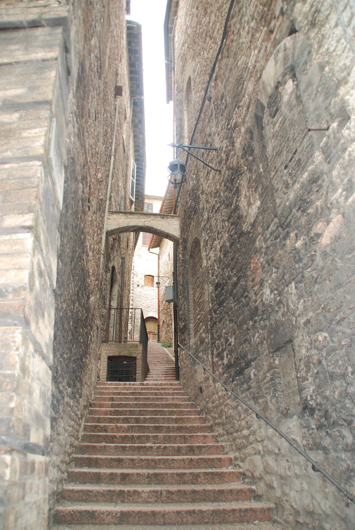 Scalinata di pietra tra vecchi muri medievali, con arco e lampione