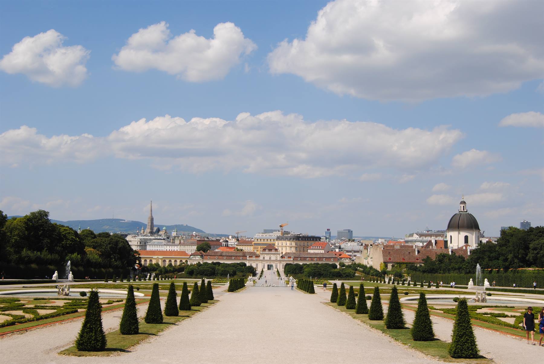 Viale con conifere simmetriche verso il Palazzo Belvedere, cielo nuvoloso su Vienna