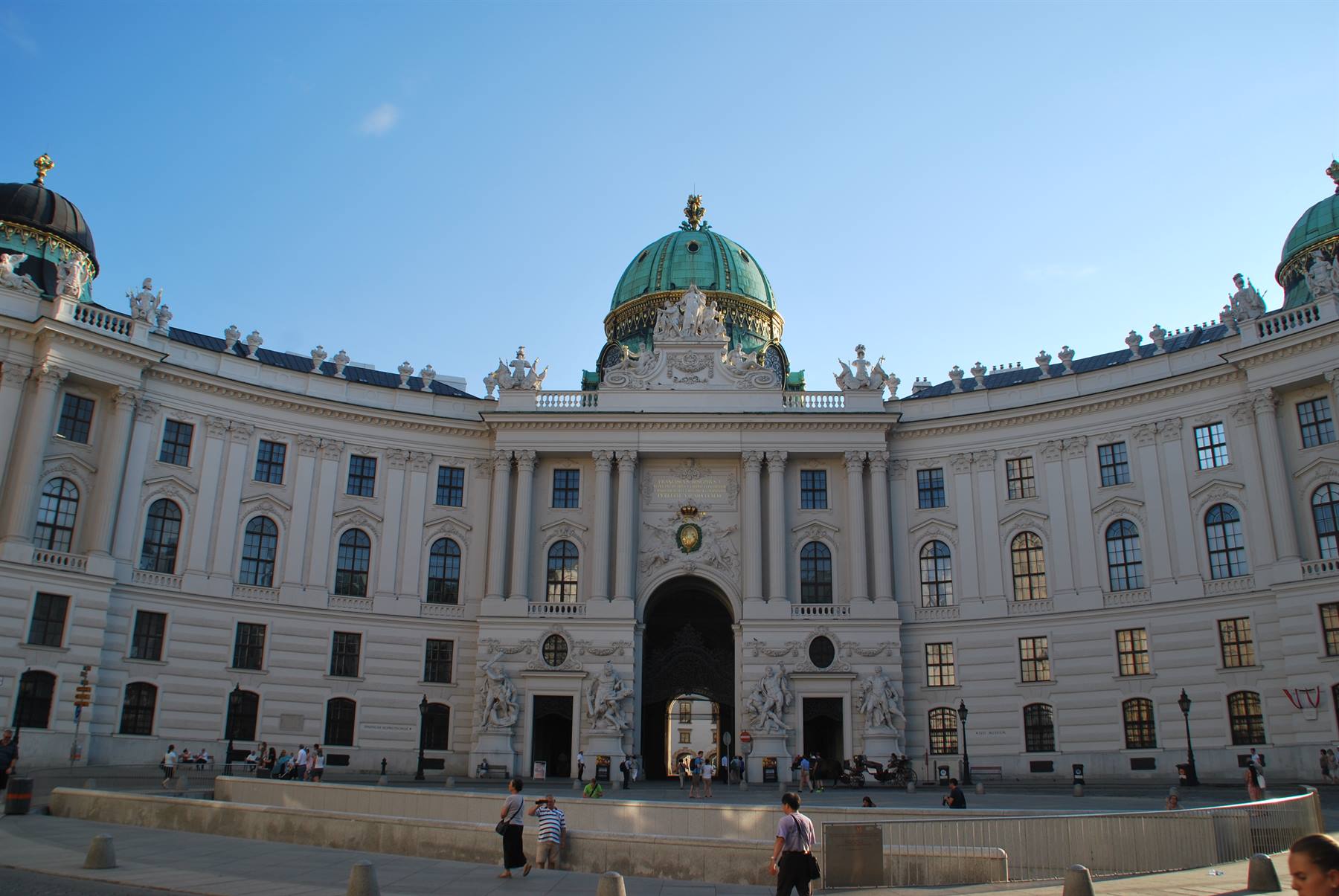Facciata bianca della Hofburg a Vienna con cupola verde e turisti in piazzetta
