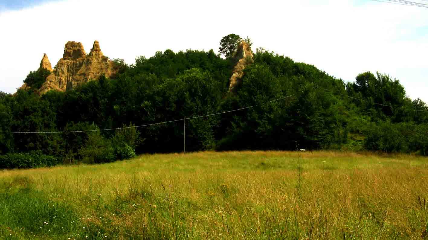 Calanchi di argilla spuntano sopra il bosco verde, davanti a un prato erboso