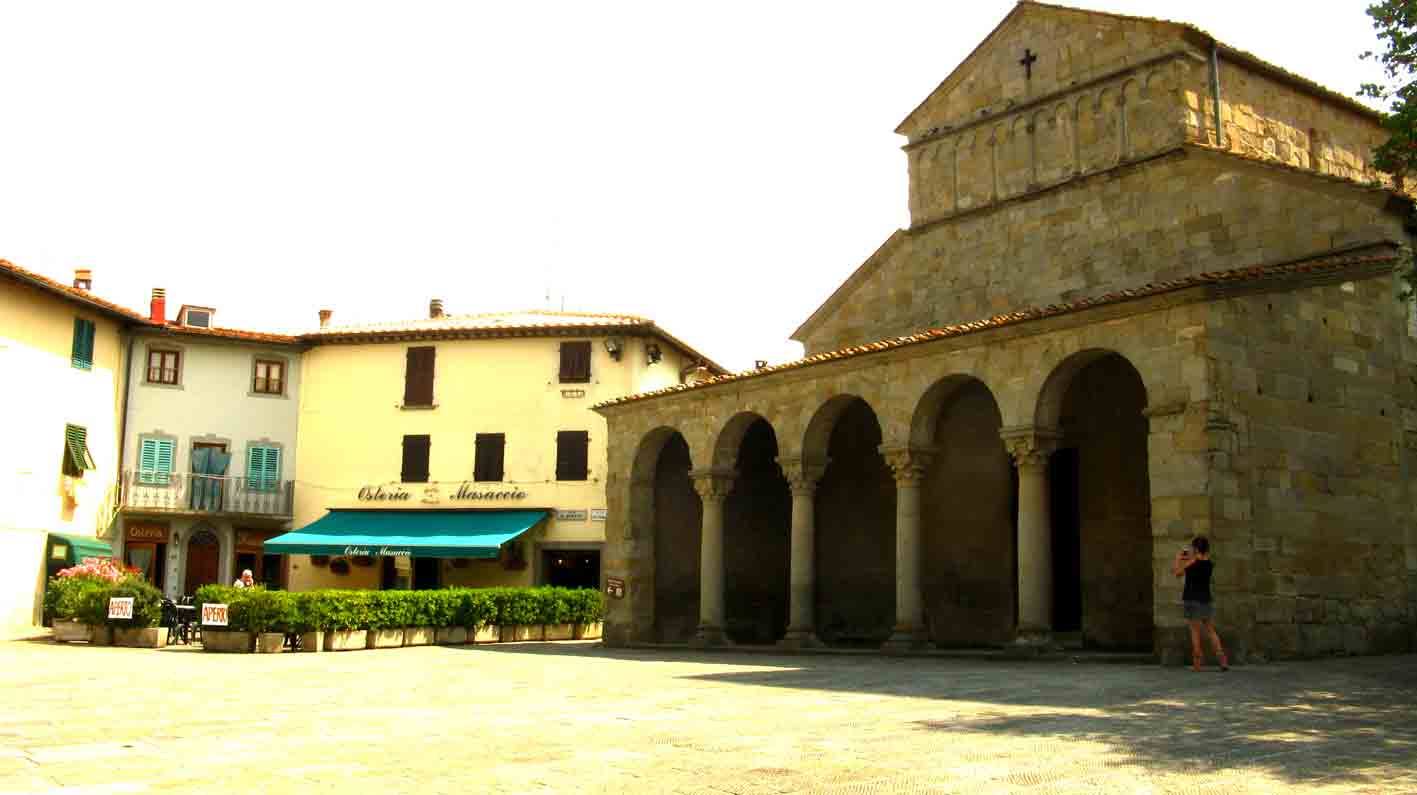Chiesa romanica in pietra con portico ad archi, donna fotografa accanto
