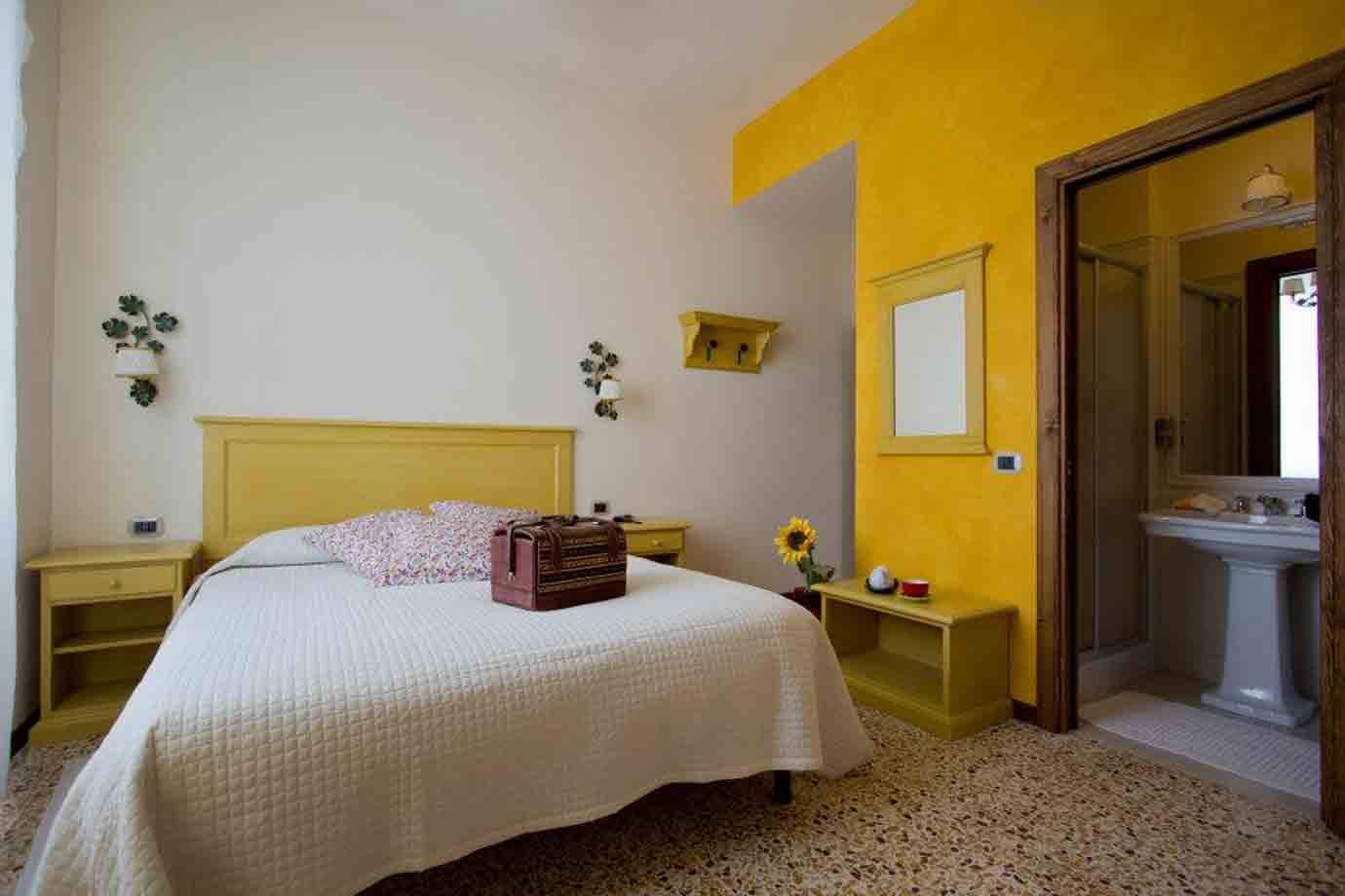 Camera d'albergo con letto giallo, valigia in pelle, muro giallo e bagno aperto
