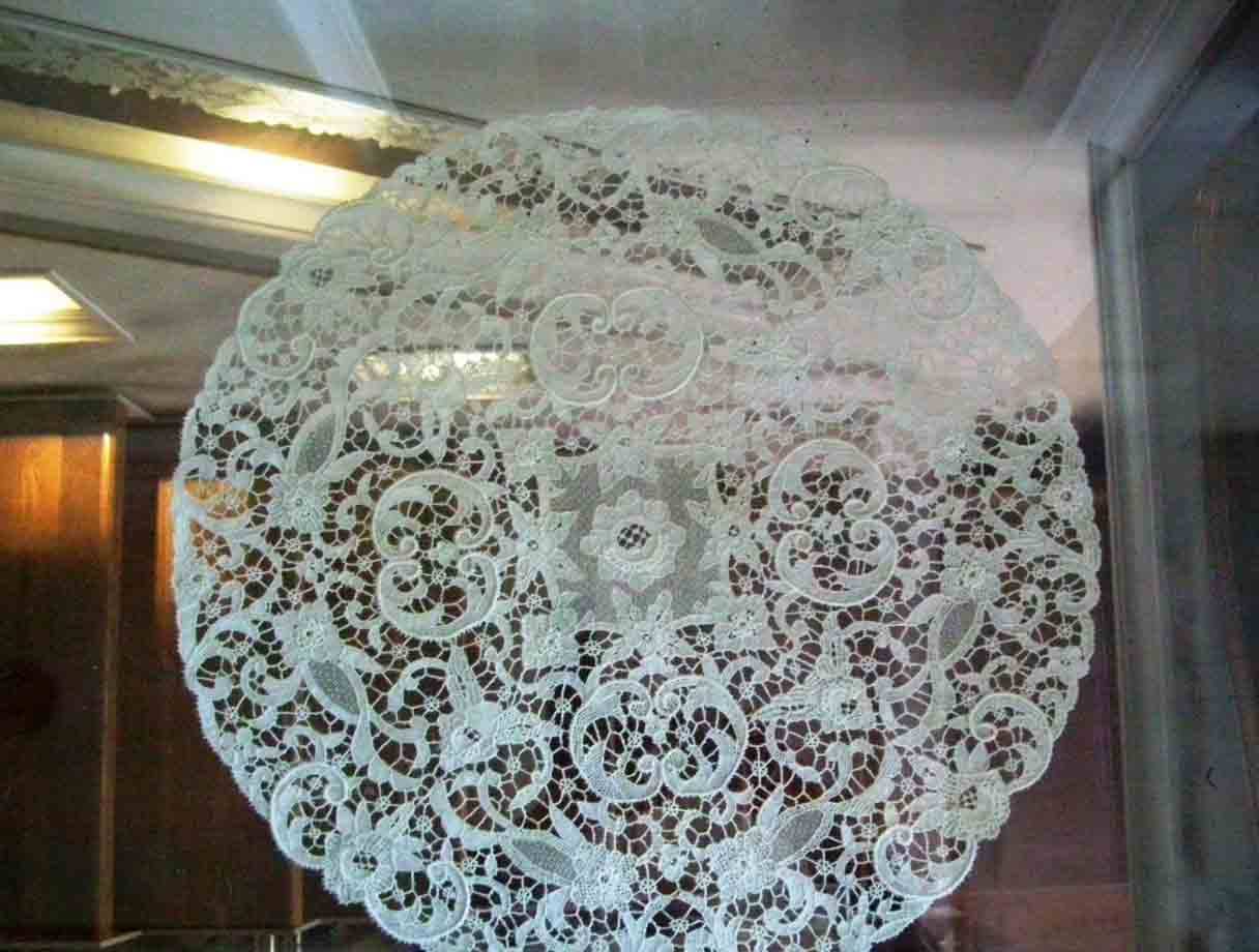 Pizzo bianco rotondo esposto dietro vetro, riflessi della luce interna